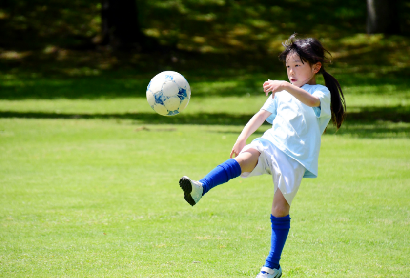 子どもが元気よく外でサッカーボールを蹴っている写真